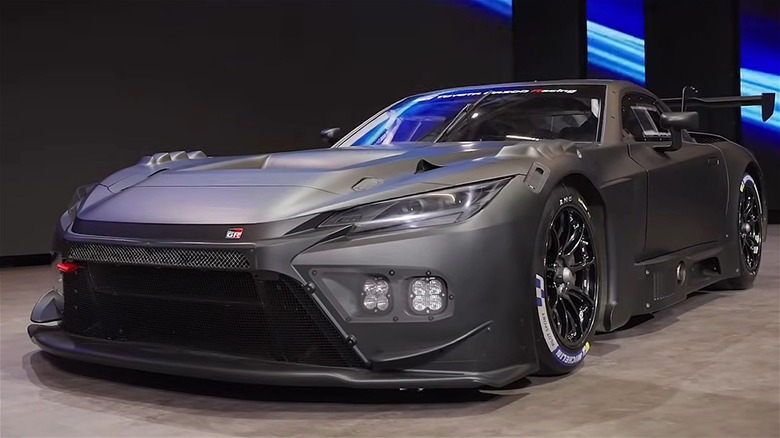 A matte-gray 2026 Toyota GR GT3 race car on display in a dimly lit showroom, rocking its extreme aero