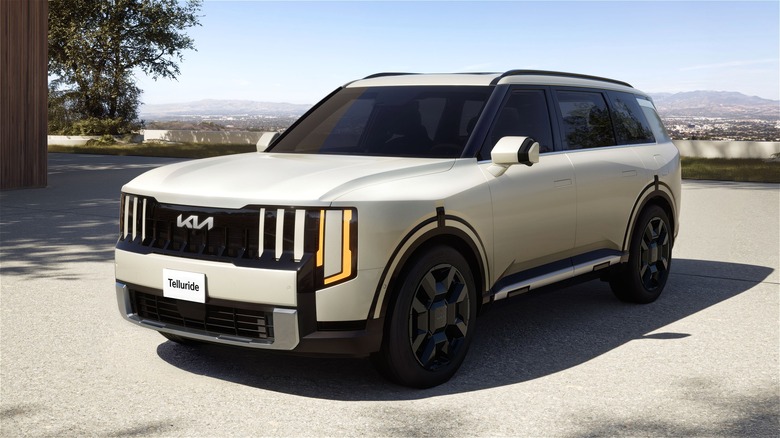 A boxy next-gen 2027 Kia Telluride HEV SXP parked in front of a modern house and tree, rocking a creamy off-white body.