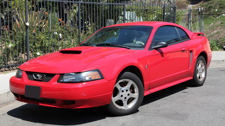 A red Ford Mustang coupe from the early 2000s parked on the street.