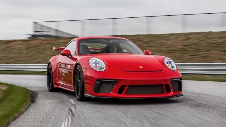 A red Porsche 911 GT3 driving on a track, viewed from the front.