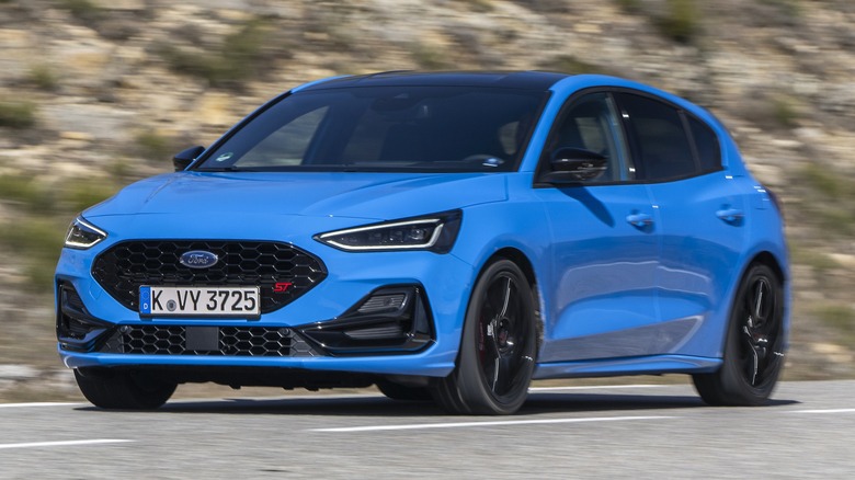 A 2024 blue Ford Focus driving on a mountain road with rocky terrain in the background.