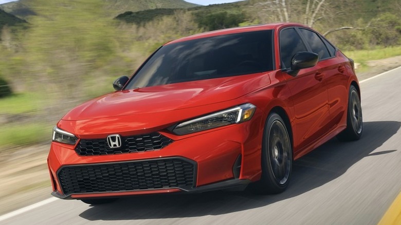 A 2025 red Honda Civic sedan sport touring hybrid speeding through a winding country road surrounded by green hills.
