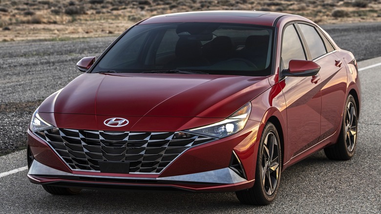 A 2026 red Hyundai Elantra driving along a desert highway with mountains in the distance under a soft evening sky.
