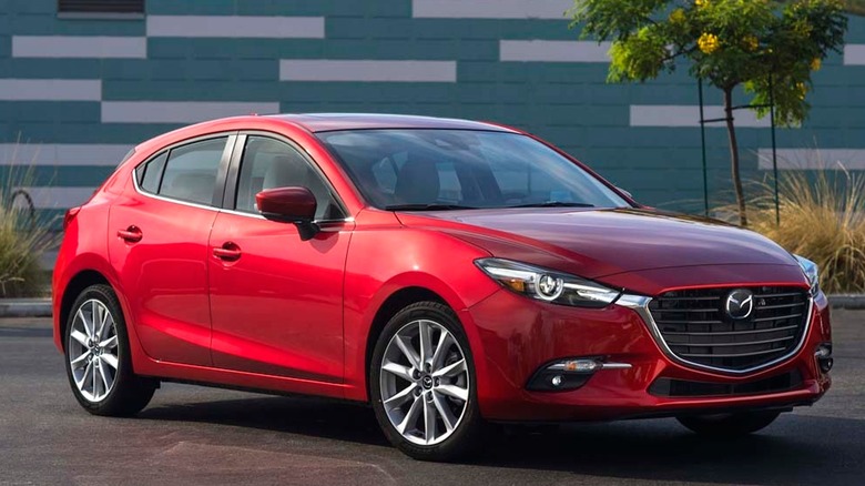 A 2017 red Mazda3 parked near a modern building with trees and plants around.