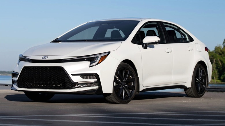 A 2026 white Toyota Corolla XSE Windchillpearl parked in an open lot with clear blue skies and greenery in the distance.