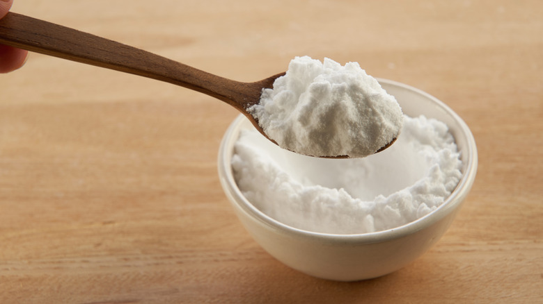 Wood spoon holding a scoop of white powder over a bowl of the same ingredient