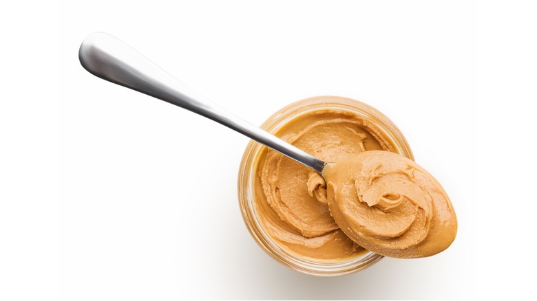 Overhead shot of peanut butter jar under a spoon containing peanut butter