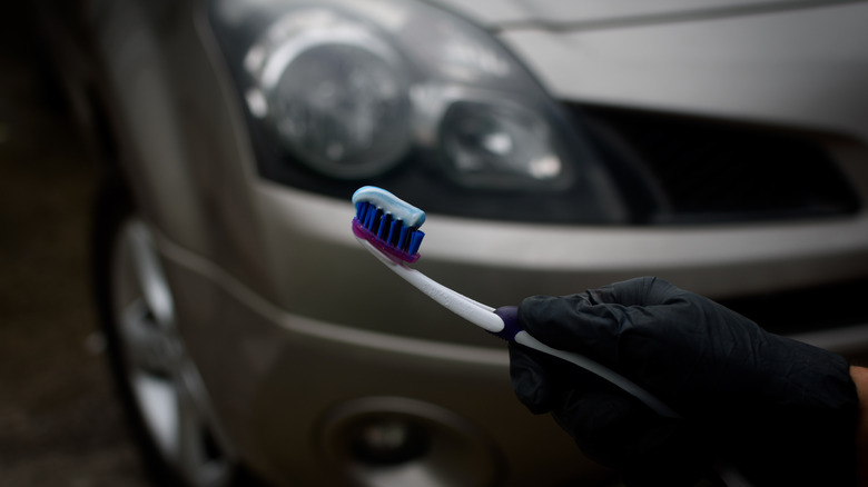 Black gloved hand holding a toothbrush with a blurred car in the background