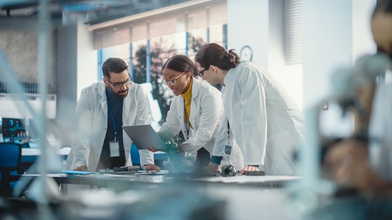 Group of scientists in white coats looking at a laptop