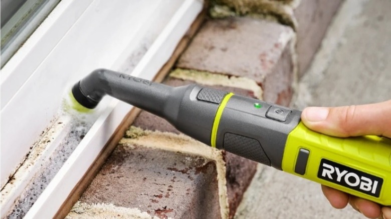 Hand using a rotating scrub brush to clean a windowsill
