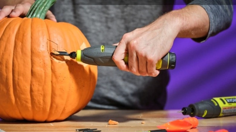 Hand using a tool to carve a pumpkin