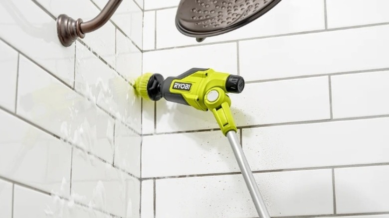 Green scrubbing tool on a pole cleaning inside a white tile shower