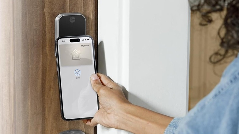 A person tapping their iPhone on the Yale lock to unlock the door