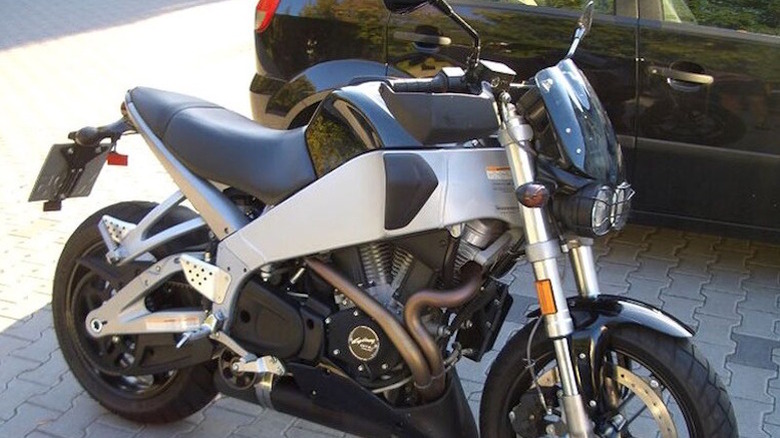 A Buell XB9SX City sitting on cobblestone with a black SUV behind it, in the shade