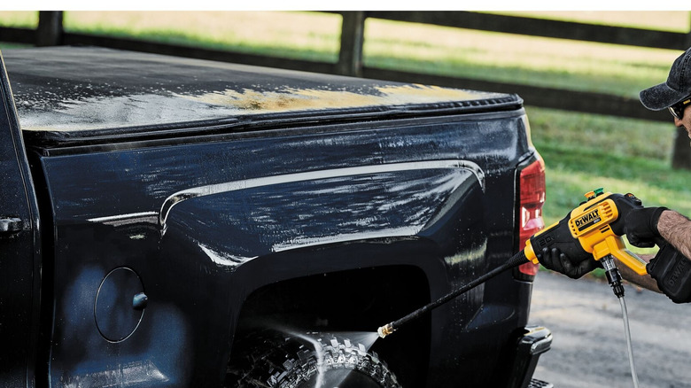 A person using a yellow DeWalt 20V MAX 550 PSI Cordless Power Cleaner to wash the wheel of a black pickup truck.