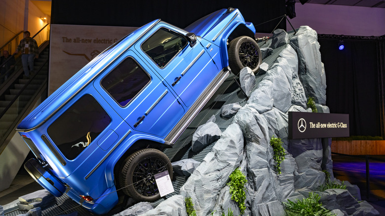 A blue Mercedes-Benz G-Class EV propped on fake rocks in a building.