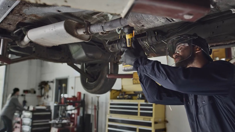 Person using grinder on a muffler under a lifted vehicle