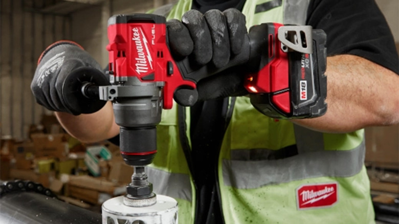 A man using a Milwaukee drill to cut a hole in sheet metal