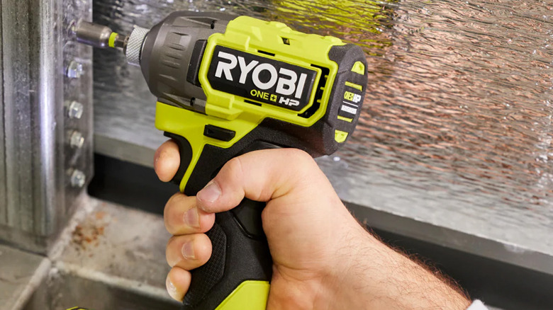 A Ryobi impact driver tightening bolts on a strip of metal.