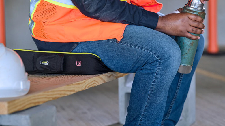 A construction worker sitting on a Ryobi heated cushion.