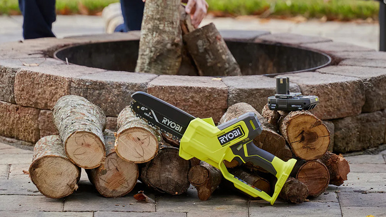 A Ryobi 6-inch chainsaw sitting next to a pile of small logs.