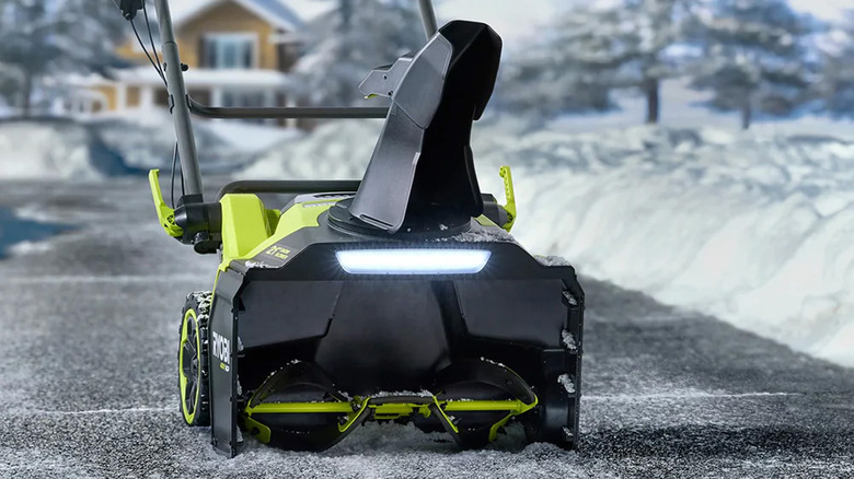 A Ryobi snow blower on a clean sidewalk surrounded by snow.
