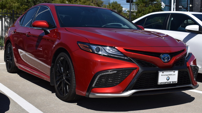 A red Toyota camry from the latest facelifted generation parked outside a dealership glass front