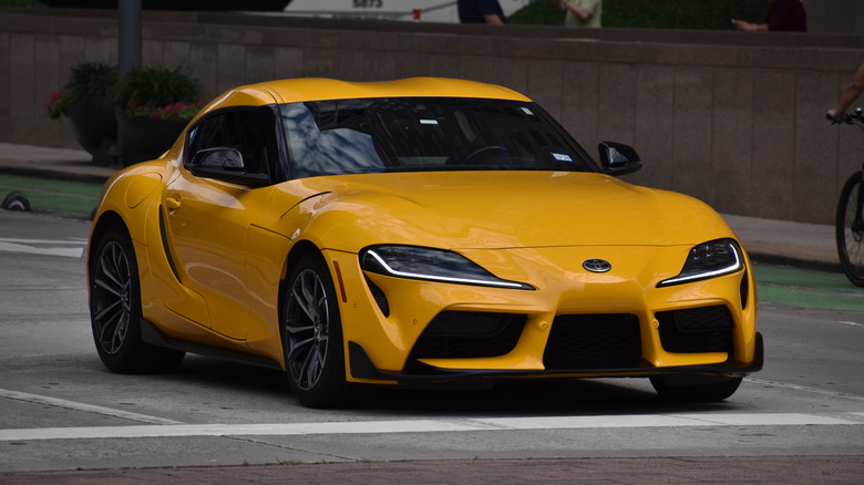 A yellow GR Supra from the Mark V generation spotted at a stop line at an intersection
