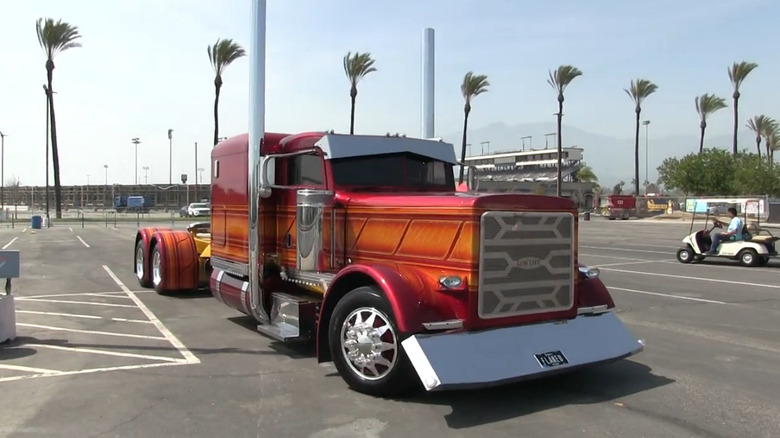A custom show semi truck with a bold red and orange gradient paint job, tall chrome exhaust stacks, and a polished chrome grille and bumper.