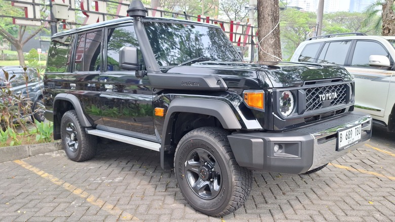 A black Toyota Land Cruiser (J70) parked in a lot alongside other vehicles, including a white one in the background.