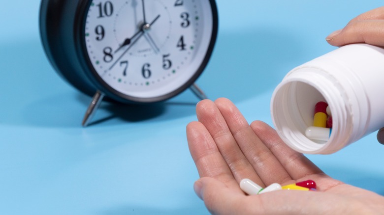 Hand and a pills bottle with a bedside clock