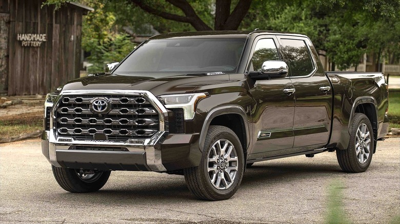 A brown 2024_Toyota_Tundra_1794_Edition_Smoked_Mesquite_054 pickup truck parked in a rustic outdoor setting near a wooden building.