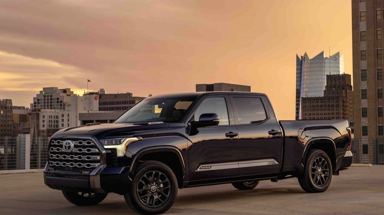 A black Toyota Tundra Platinum pickup truck is parked on a rooftop with a city skyline in the background at sunset.