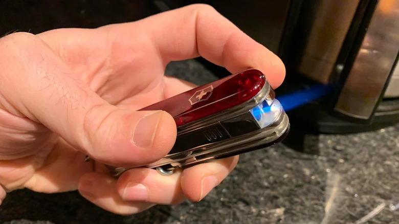 A person holding a red Swiss Army knife with an integrated butane torch, emitting a blue flame over a dark countertop.
