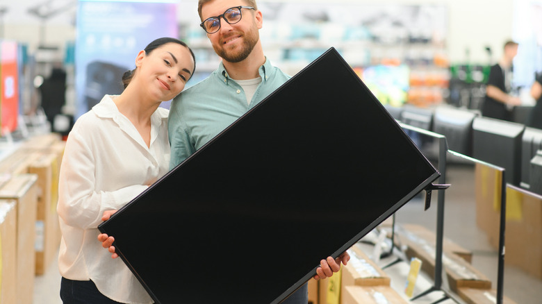 Two people hold a plasma TV in a store.
