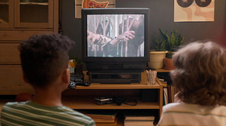 Back view of two kids watching a movie on an old TV.