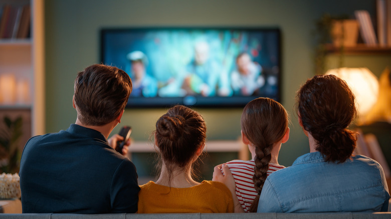 Four people watch TV on a sofa, TV is blurry.