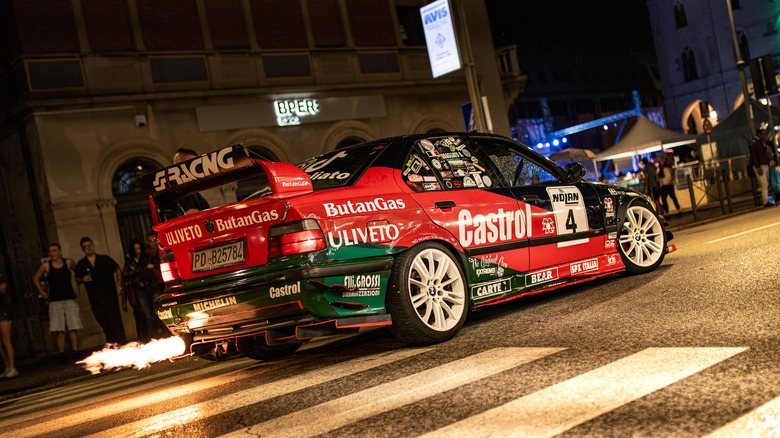 A red, black, and green tuned race car on a city street, with flames coming out of the exhaust.