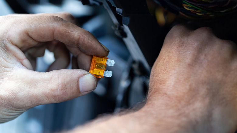 A close-up of a person putting a new fuse into a car's fuse box.