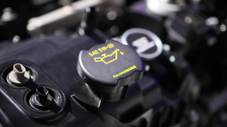 A close-up of a car's oil cap on an engine. The cap says SAE 5W-20 Recommended and has a picture of an oil can on top.