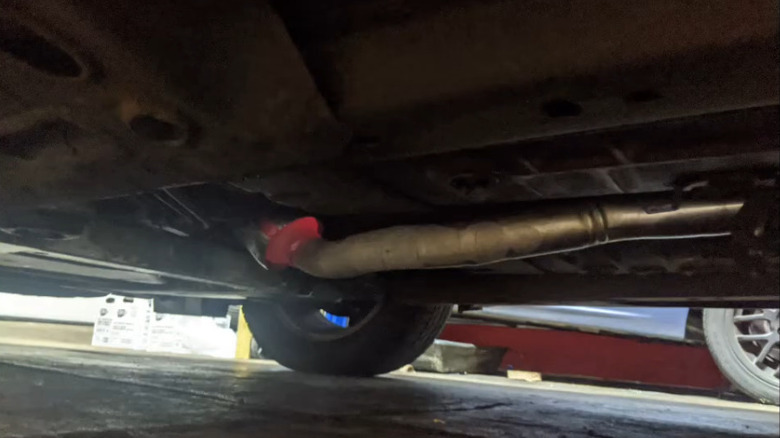 A view from underneath a car showing part of the exhaust system with a catalytic converter glowing red hot.