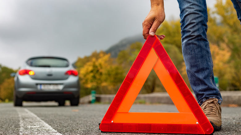 A person putting down a safety triangle behind their car that's stalled on the road.