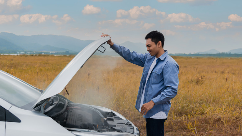 A person in front of their car with the hood up, staring at the smoke coming from the engine.