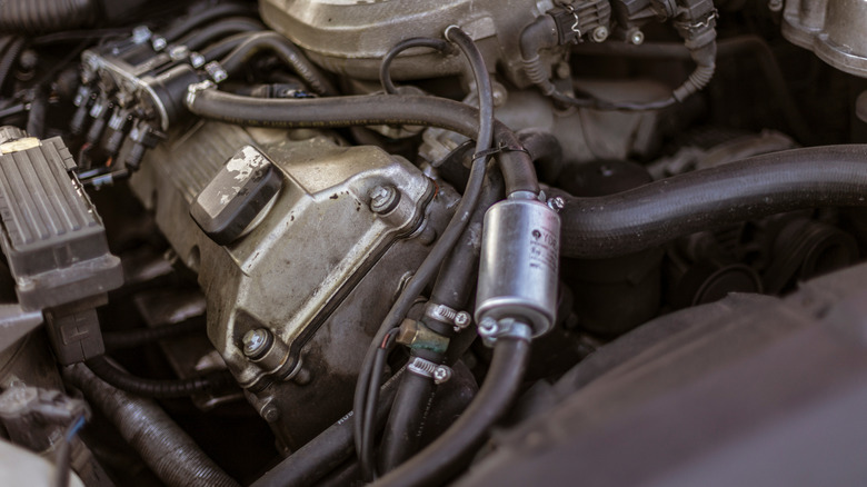 A close-up of a car's engine, highlighting its various old hoses and other lines.