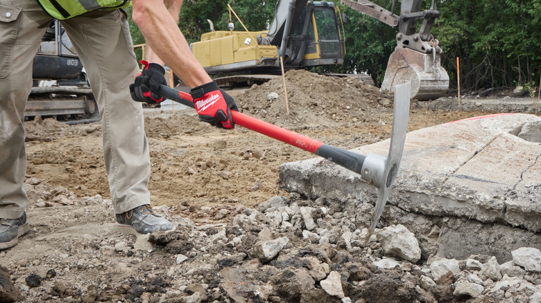 A worker breaking concrete with a Milwaukee pick mattock.
