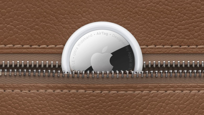 Apple AirTag peeking out of a zippered pocket on a brown textured background.