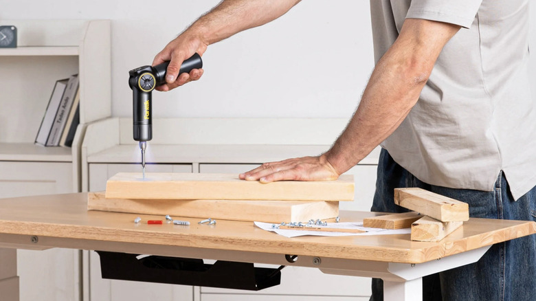 Person using the Fanttik electric screwdriver on a plank of wood on top of a worktable.