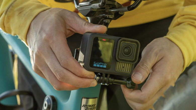 Person adjusting a black GoPro camera beneath a bicycle seat.