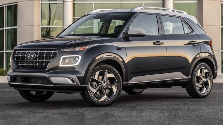 A black 2025 Hyundai Venue parked on a paved surface outside a modern glass building.