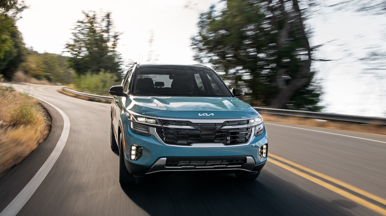 A blue 2025 Kia Seltos driving on a winding roadway.